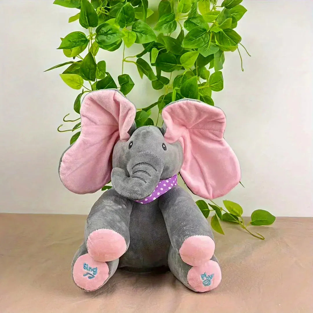 Soft grey elephant plush toy with oversized pink ears and a purple polka-dot scarf, sitting in front of green leaves – ideal for sensory play and cuddles.